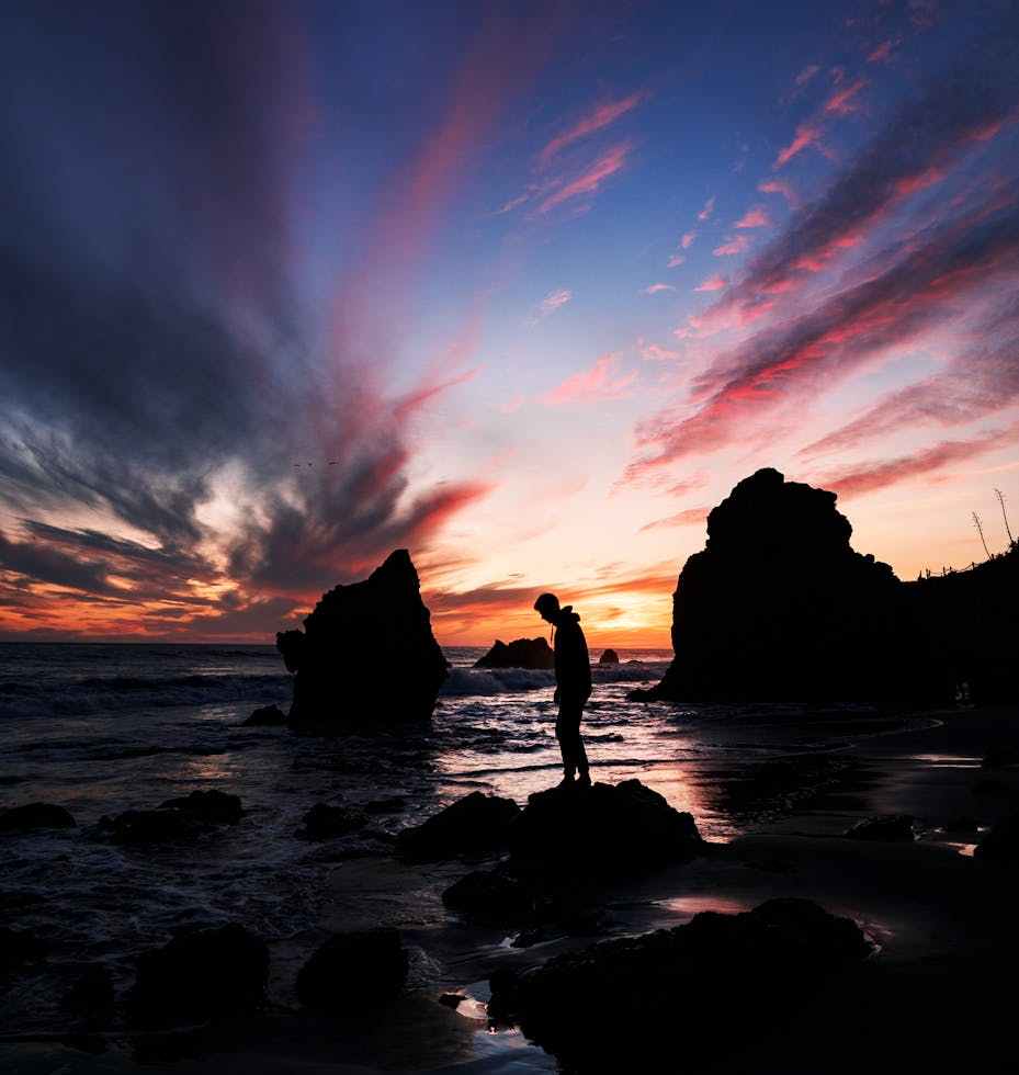 person standing on a rock by the seashore at sunset