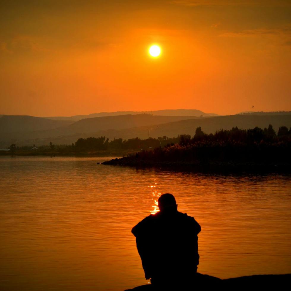 silhouette of person sitting beside body of water